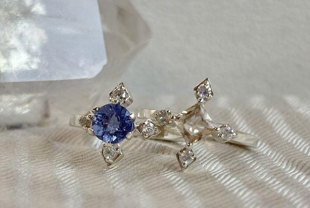 compassシリーズより、ブルーのカラーチェンジフローライトが中石のCelestiaとシャンパンカラーのオレゴンサンストーンが中石のLuciaが二つ並んでいる写真。